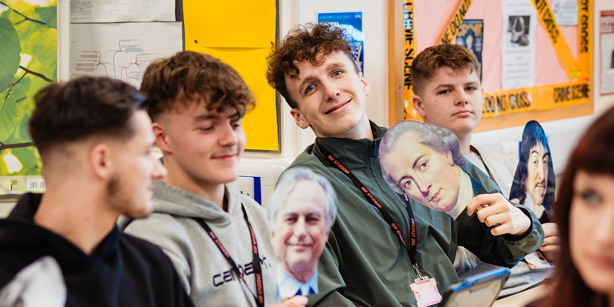 Philosophy students holding up pictures of philosophers